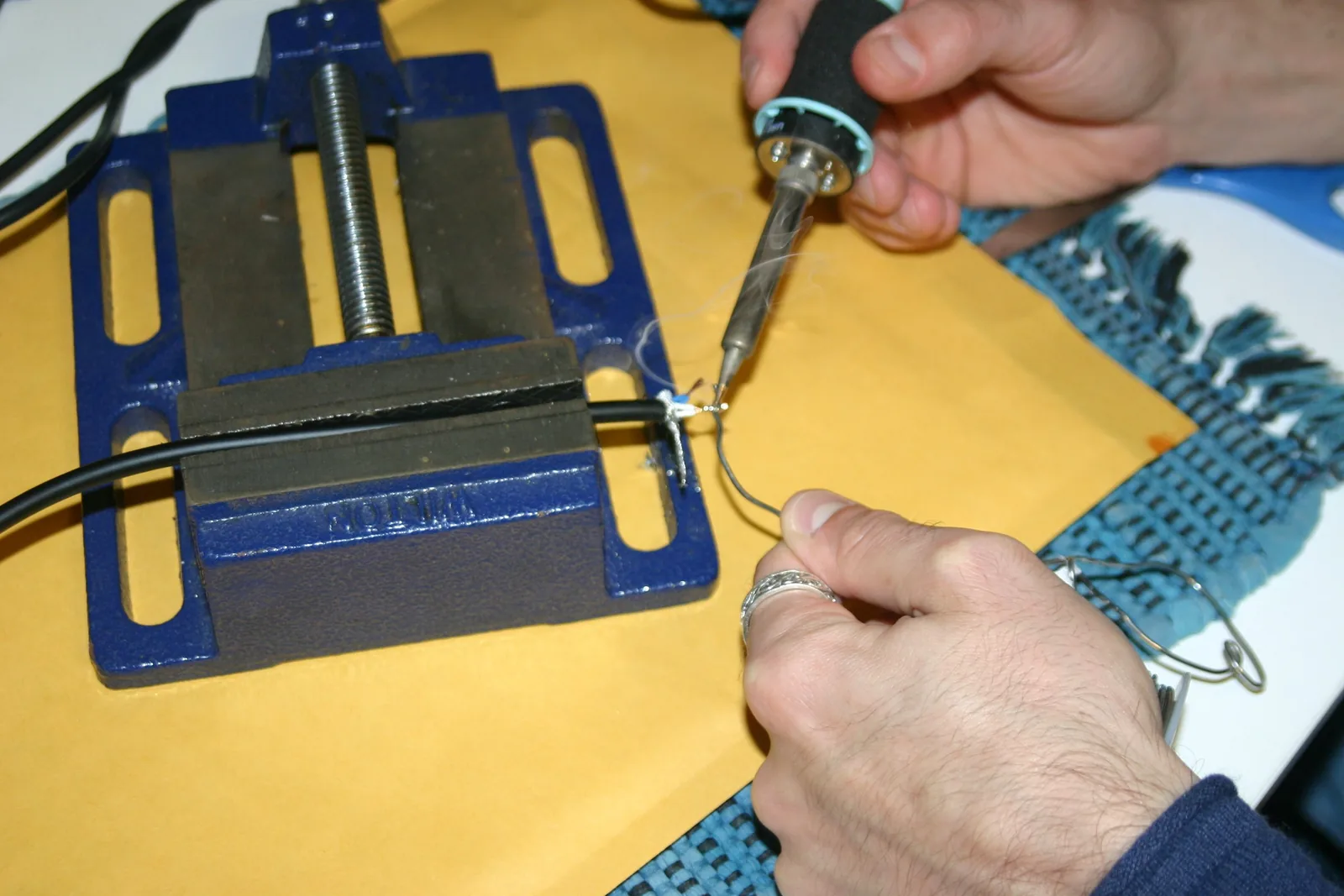 Photo of a cable clamped in a vise with a soldering iron applying a thin coat of solder to each stripped conductor during the tinning step.