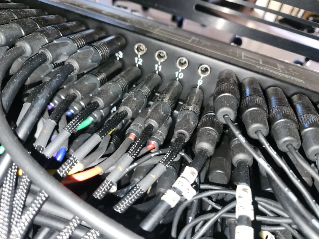 Photo of the rear panel of a TRS patchbay showing rows of numbered quarter-inch jacks with cables plugged into various connections.