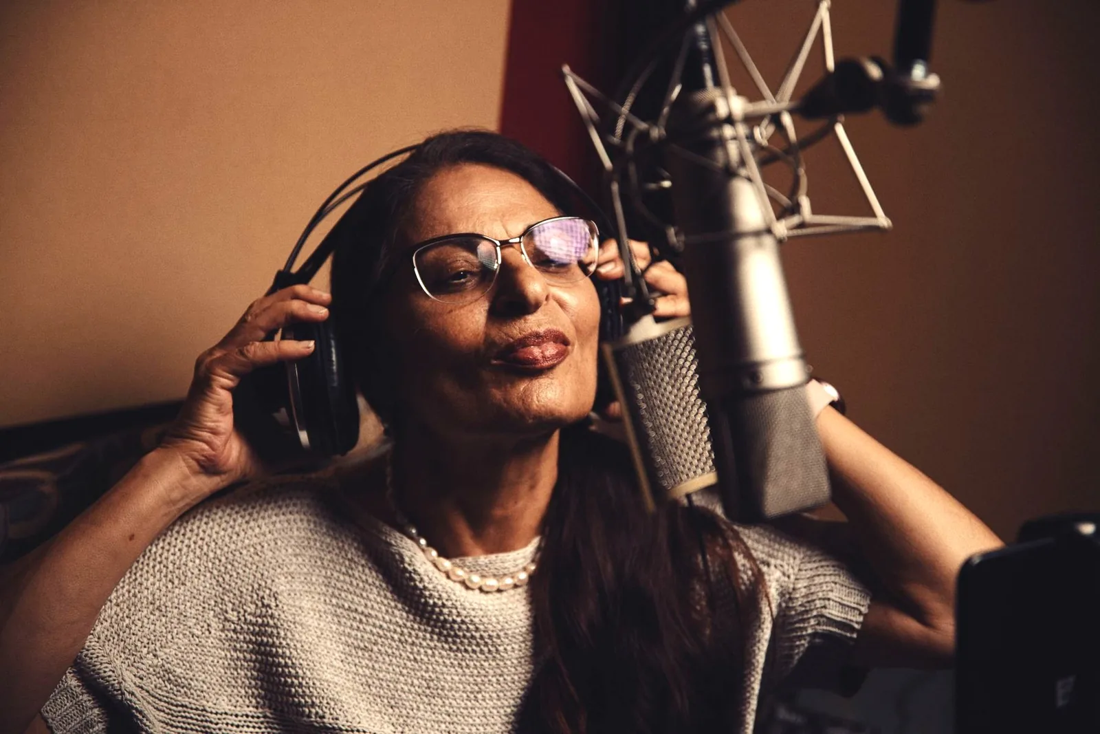 Photo of a vocalist in a tracking session, shown close up at a large-diaphragm condenser microphone while wearing headphones.