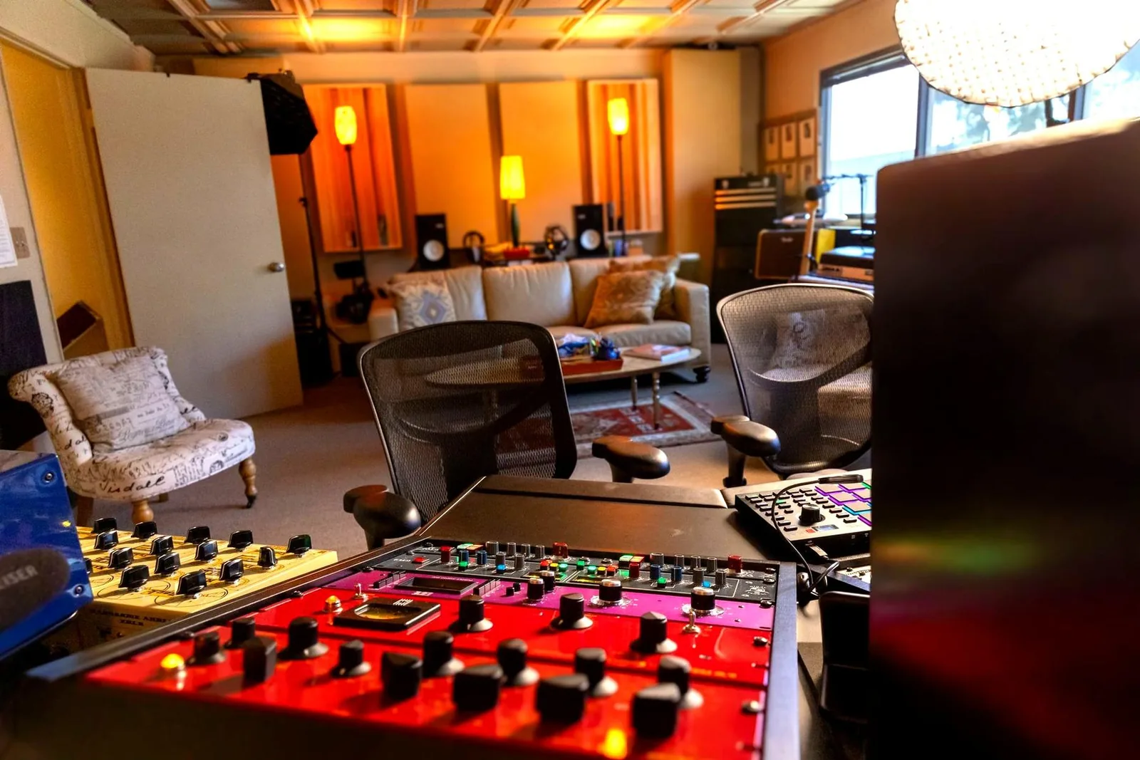 Photo of a professional studio control room viewed from behind the console, with the mix position, monitors, and equipment racks visible in the foreground.