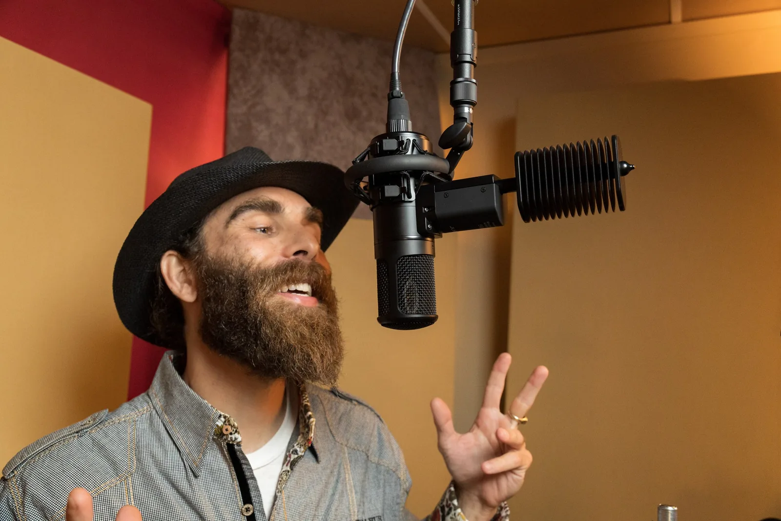 Photo of a vocalist performing in the OC Recording Company vocal booth, with heavy acoustic treatment panels visible on the wall behind the microphone.